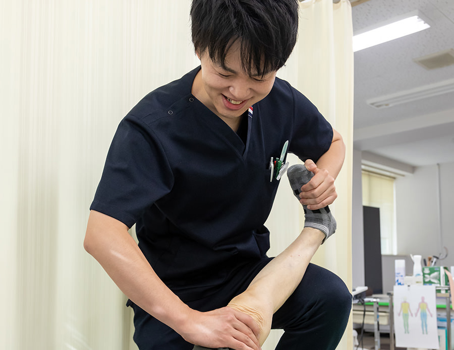 専門学校附属接骨院で、患者さまの足を持ち上げて施術する院長