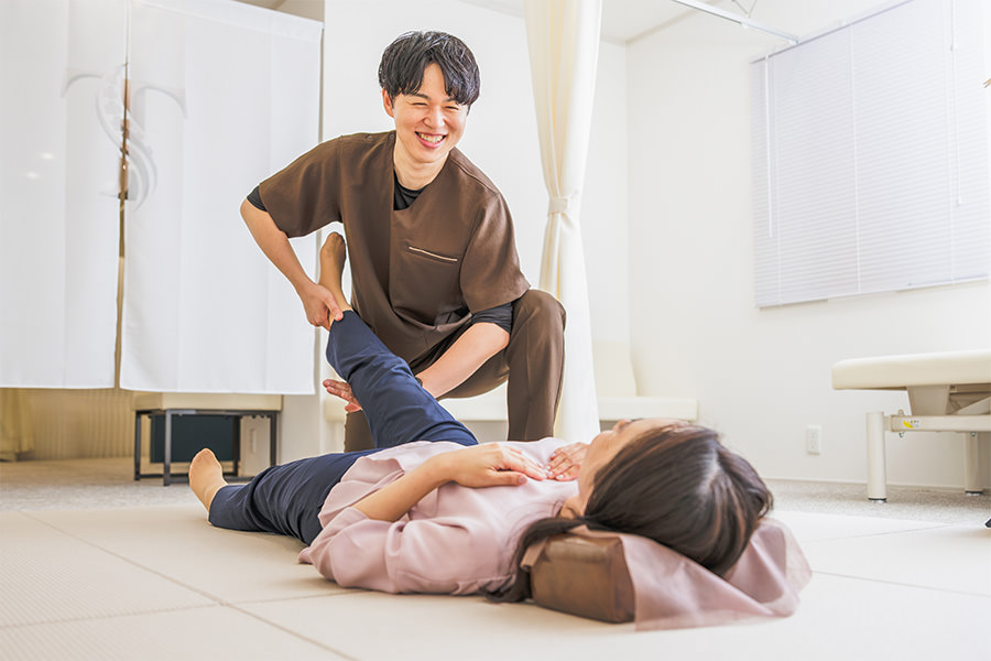 畳の上で仰向けになった患者さまの脚を持ち、笑顔で声をかける院長