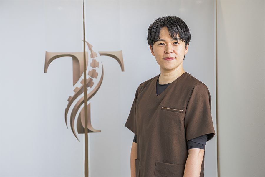 院のロゴが入ったのれんの前に立つ院長・髙野正和