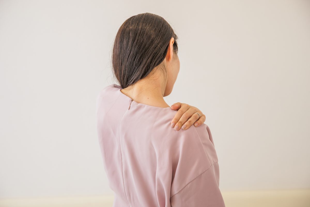 背中を向けて、片手を肩に当てる女性