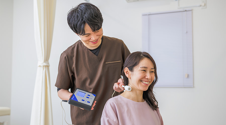 立った姿勢の患者さまの首に機器の電極を当てる院長