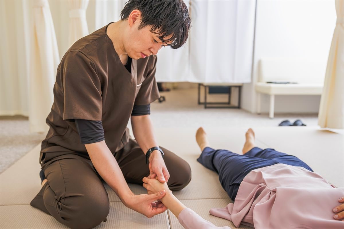 畳の上で、仰向けになった患者さまの手首に手を添えて調整する院長