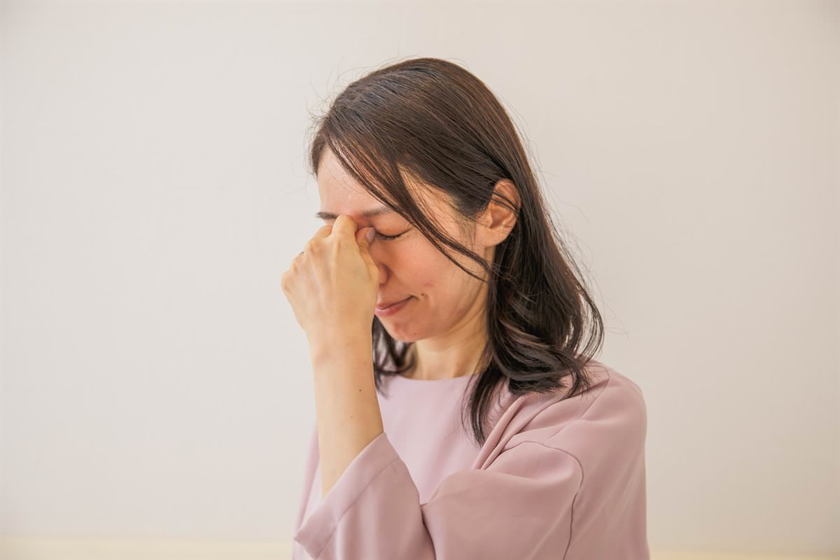 目を閉じて眉間を指で押さえる女性