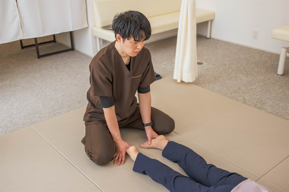 畳の上に正座し、仰向けになった患者さまの足首に手を添える院長