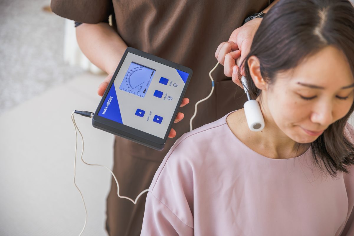 NEUBOX本体を手に、患者さまの首すじに円筒形の電極を当てている様子