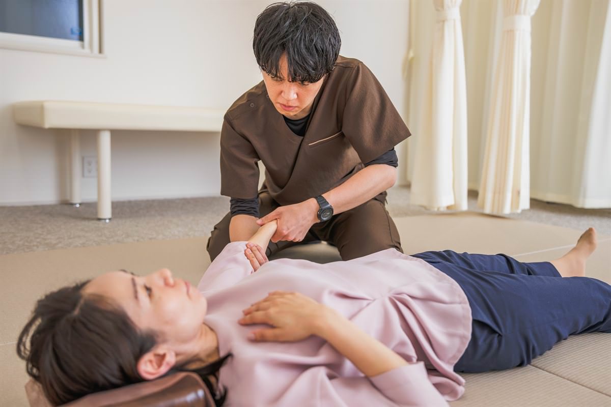 畳の上で仰向けになった患者さまの手首を持ち、優しい力で調整する院長