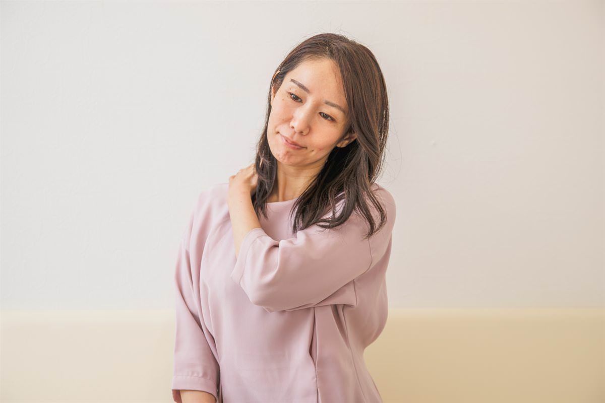 首の付け根に手を当て、つらそうに首をかしげる女性