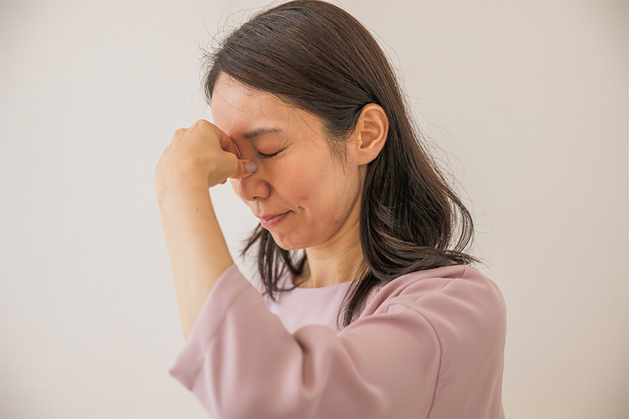 眉間に手を当て、つらそうに目を閉じる女性