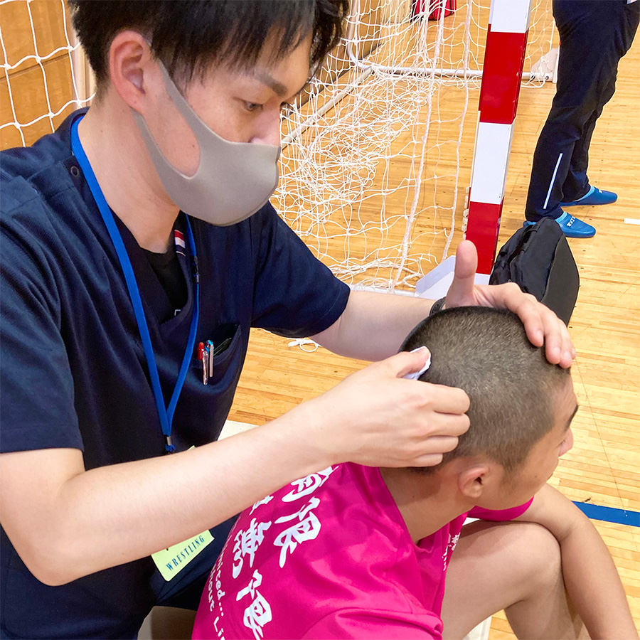 競技会場で、座った選手の頭に手を添えて施術する院長