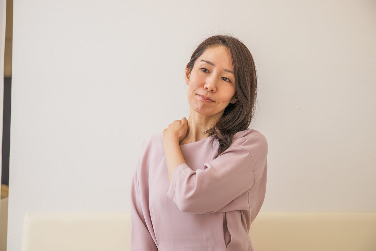 首をかしげ、片手を肩に当てる女性