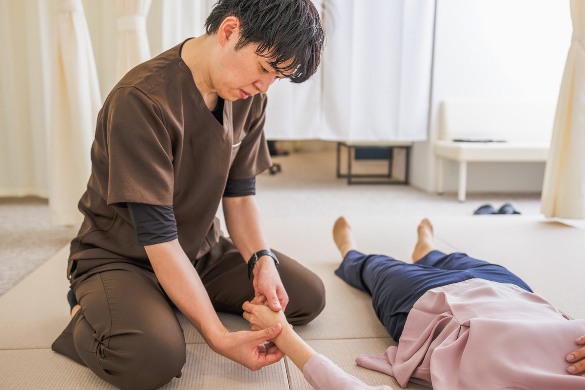 畳の上に正座し、仰向けになった患者さまの手首を両手で支える院長